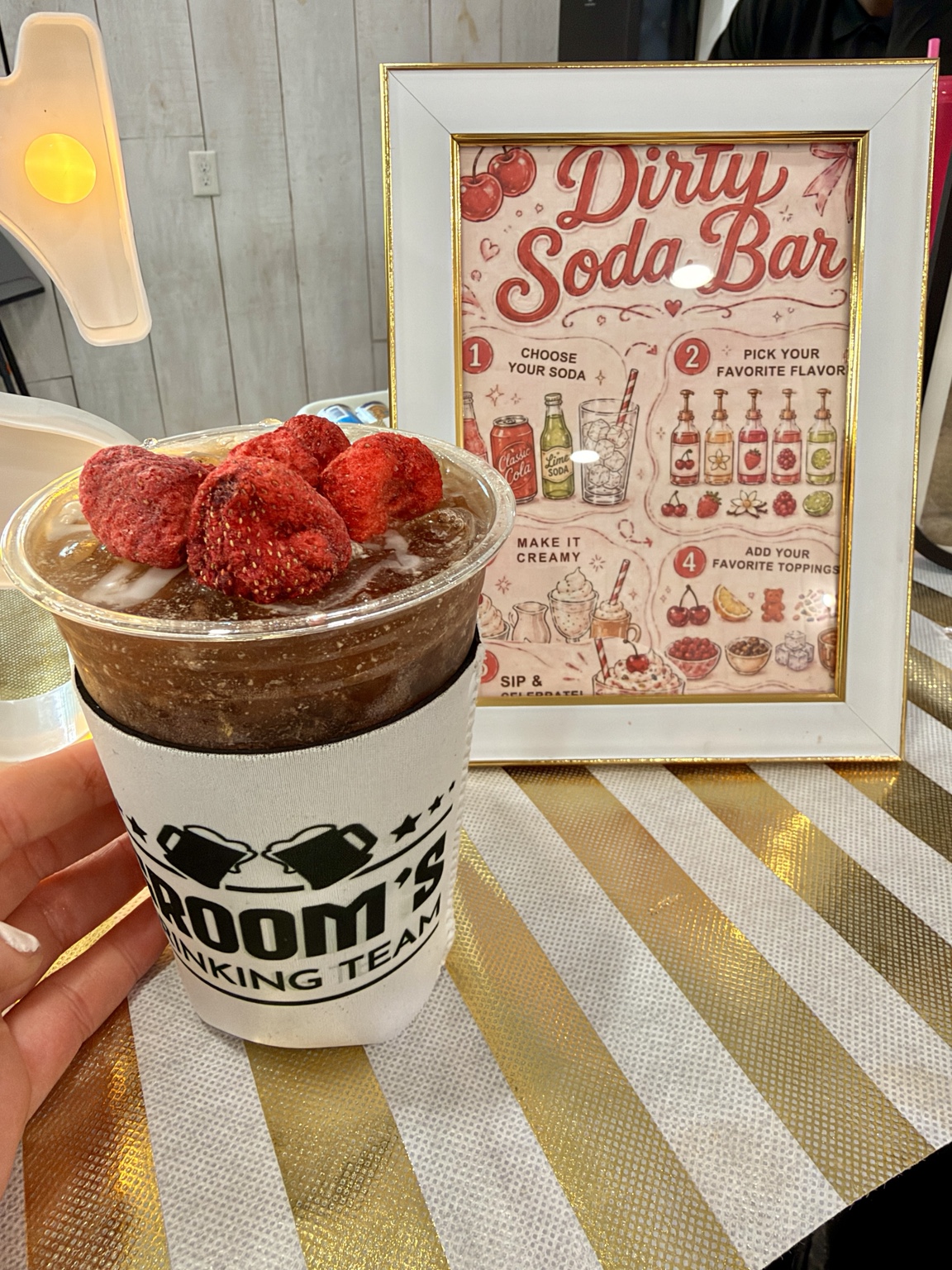 Luxury Dirty Soda topped with fresh strawberries beside a framed Dirty Soda Bar menu